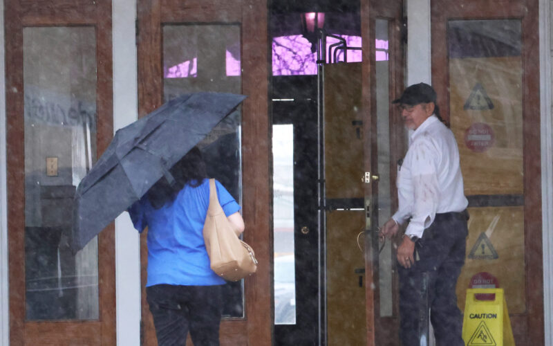 Picture of a gentleman holding the courthouse door open for a lady with an umbrella during rain.