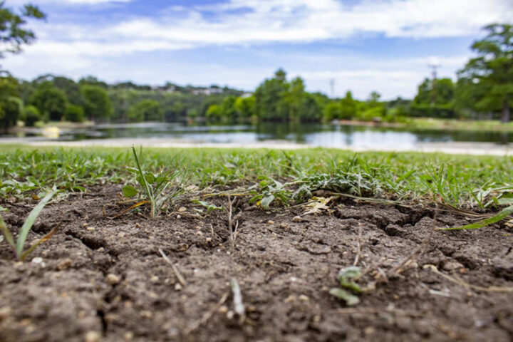 Dry cracked ground is pictured in front of the Comal River on July 18, 2025