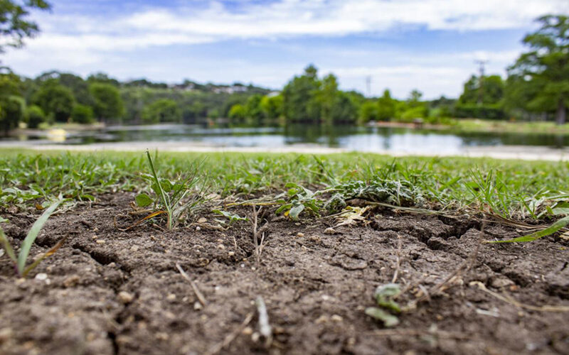 Dry cracked ground is pictured in front of the Comal River on July 18, 2025